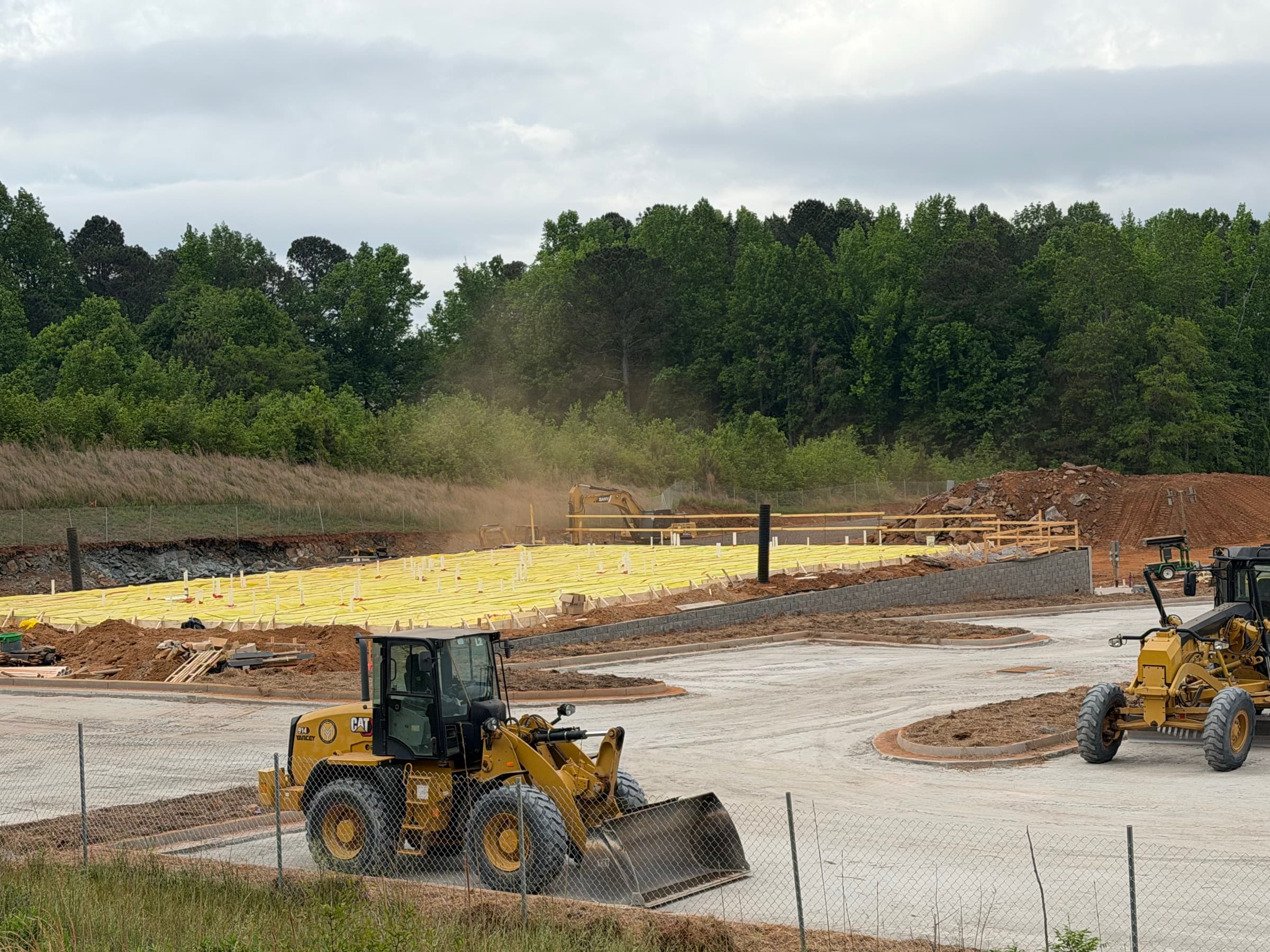 Commercial pad and slab preparation with red clay grading, equipment, retaining walls, and foundation protection.