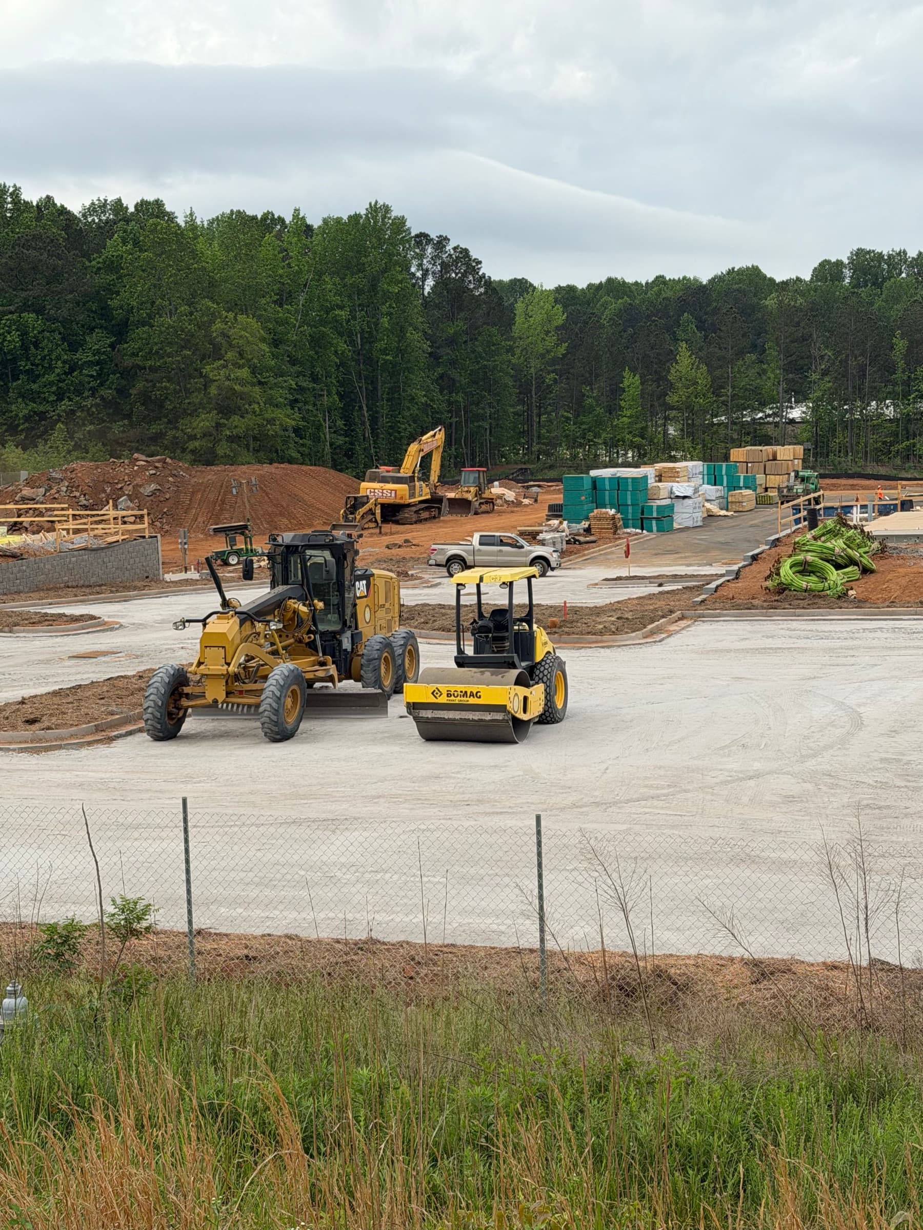 Excavator and compacting equipment working across a commercial site with red clay grading and material staging.