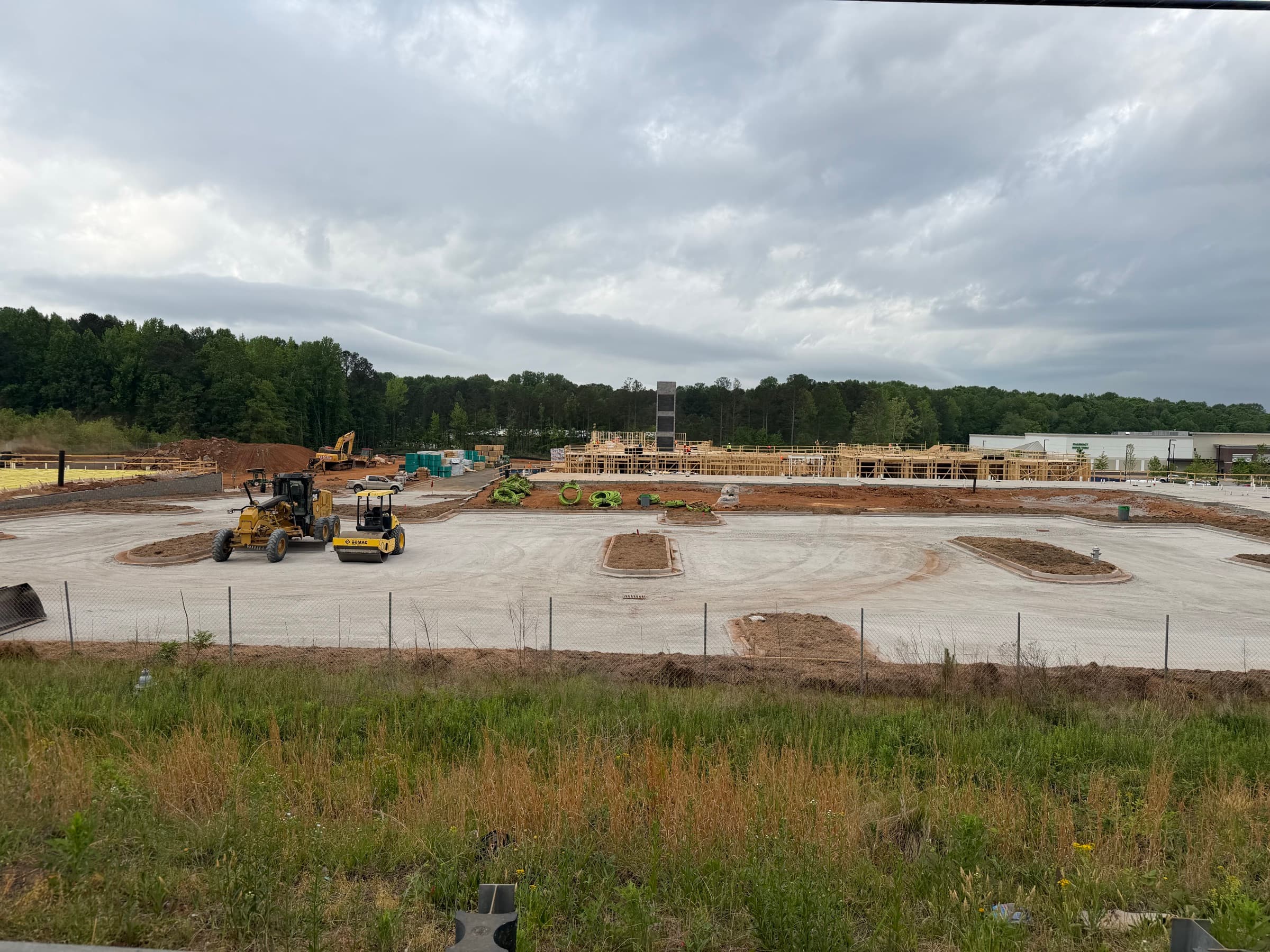 Wide view of a Peachtree Corners commercial site with grading equipment, red clay earthwork, concrete drives, and building framing.