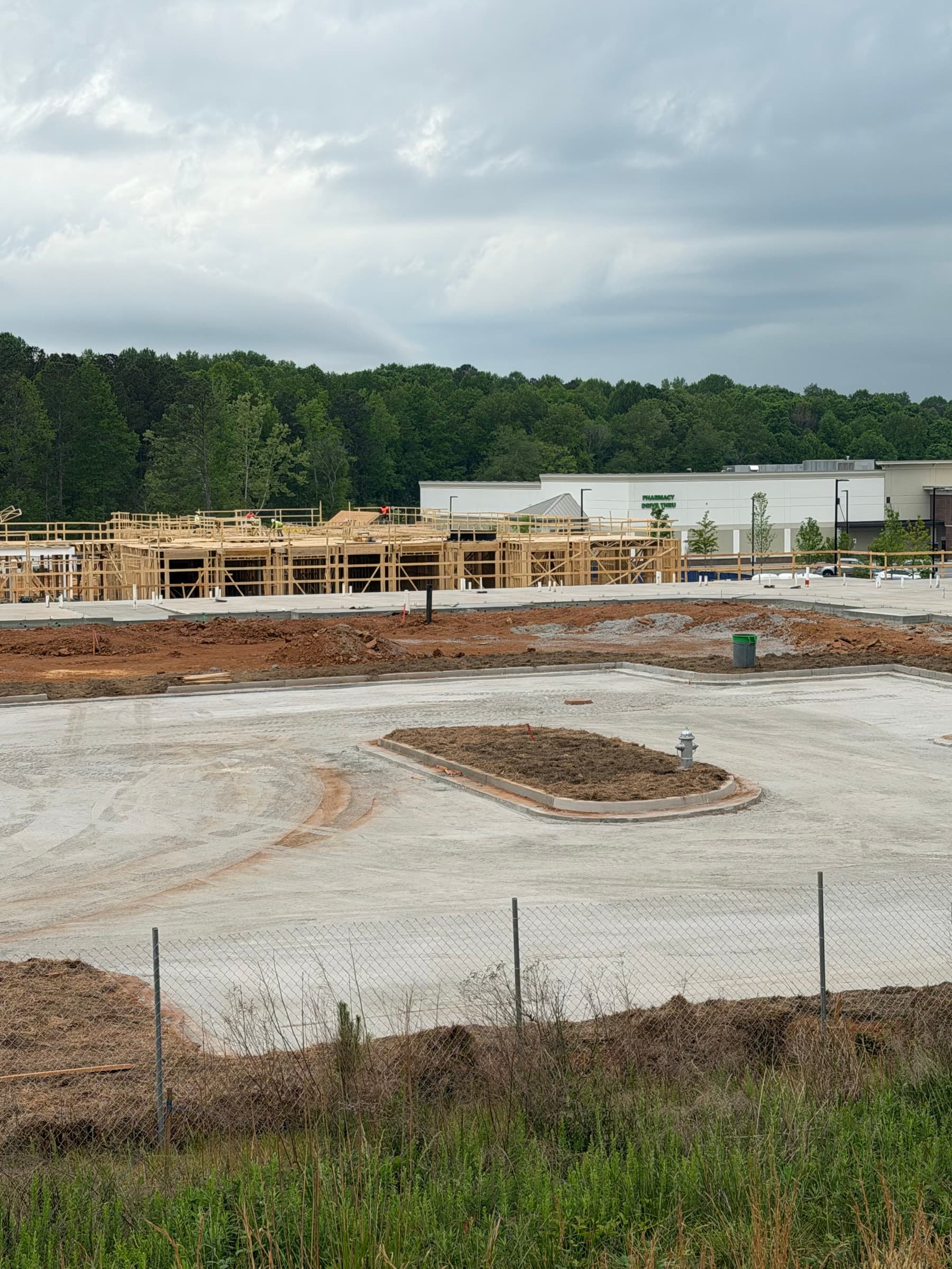 Pharmacy drive-through site with concrete base, curb islands, red clay grading, and building framing underway.