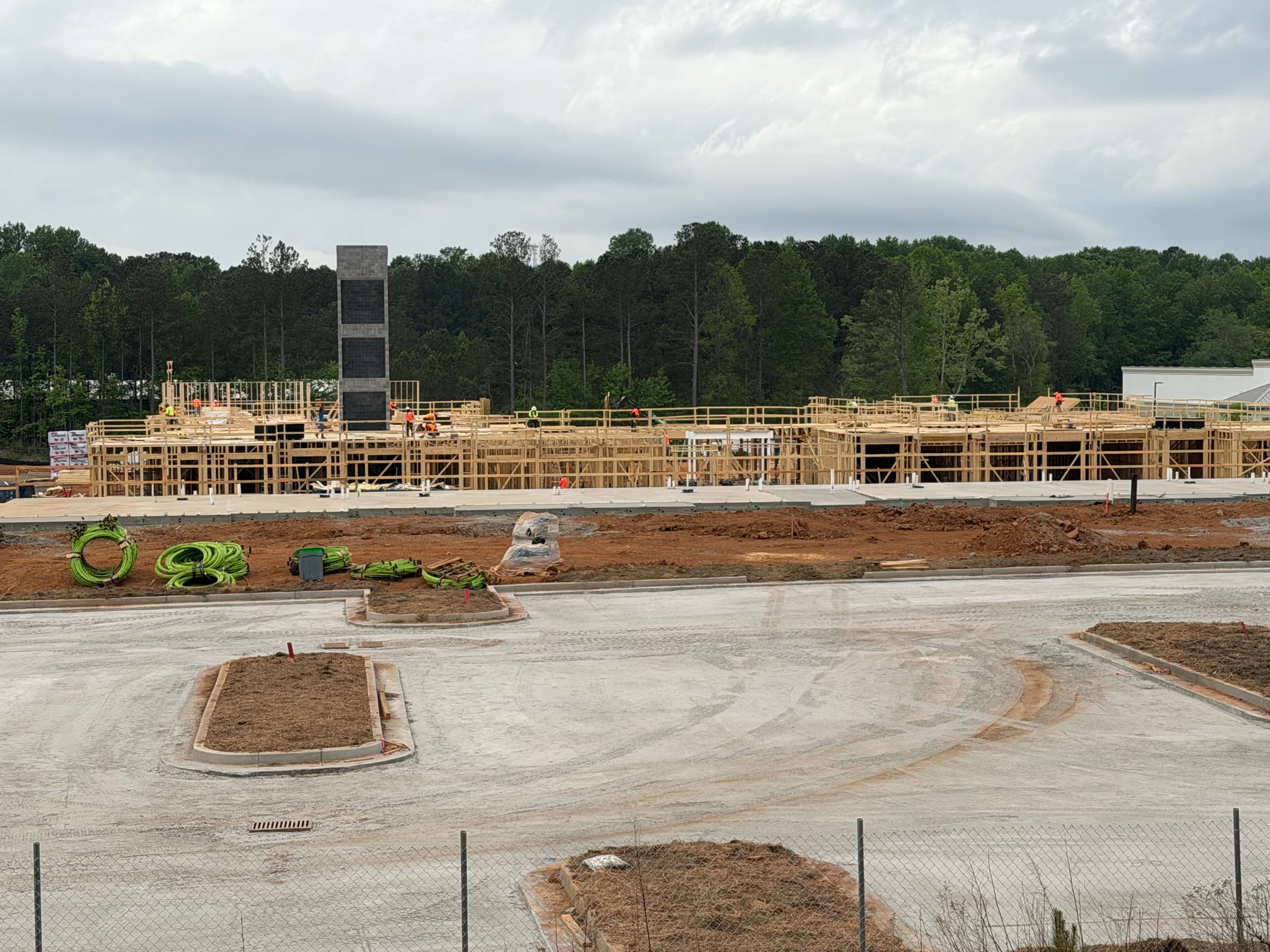 Pharmacy drive-through framing with green utility conduit staged beside concrete drives and red clay sitework.
