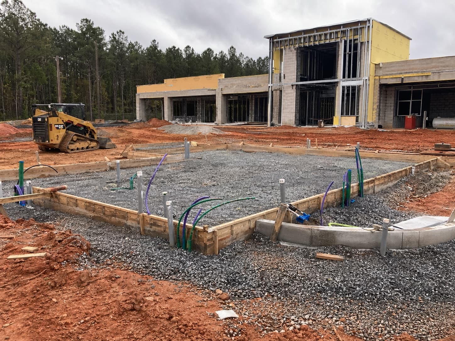 Commercial slab prep with utility conduit, gravel base, curb work, and compact equipment.